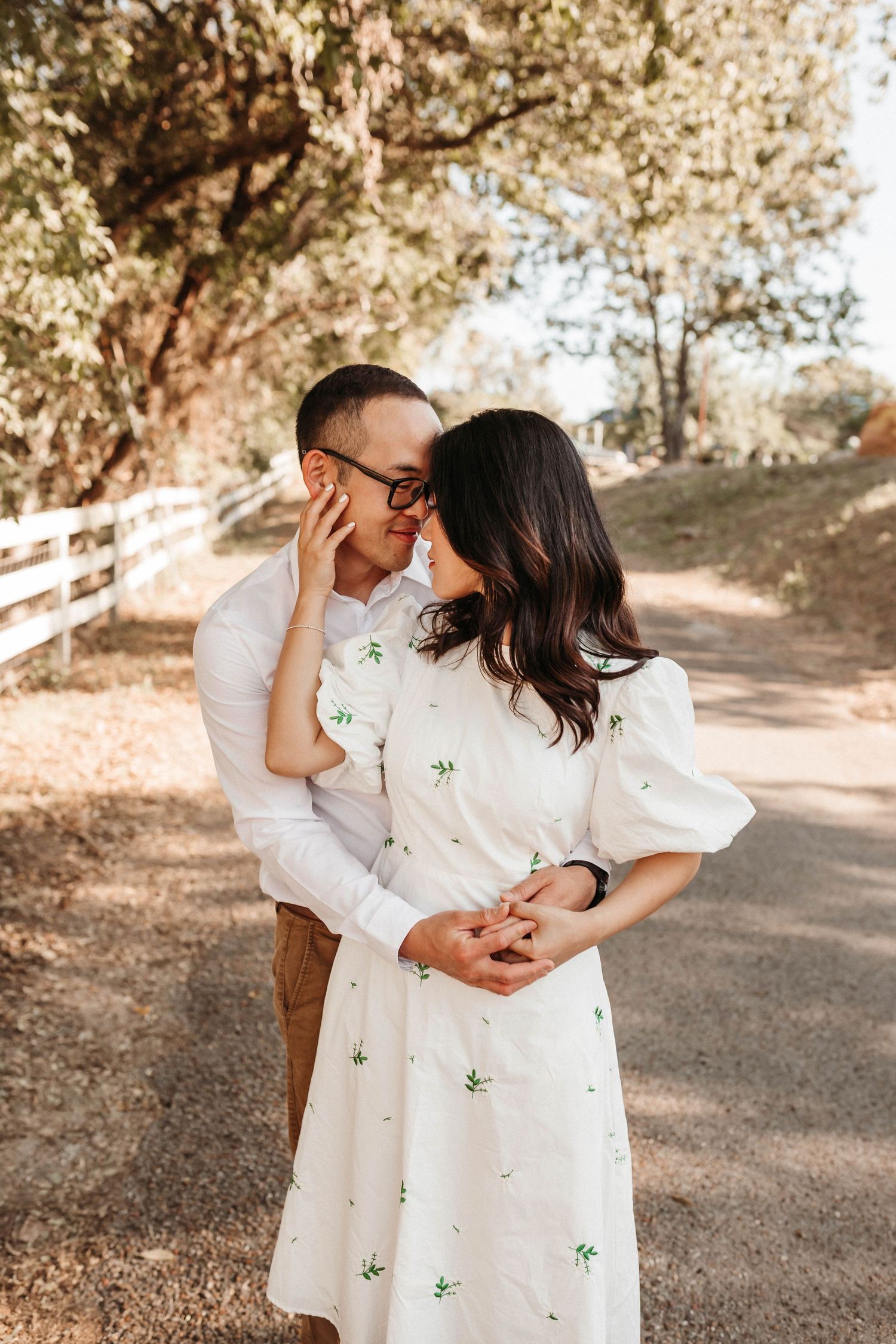 A tender moment between a couple in white outfits captured under dappled sunlight.