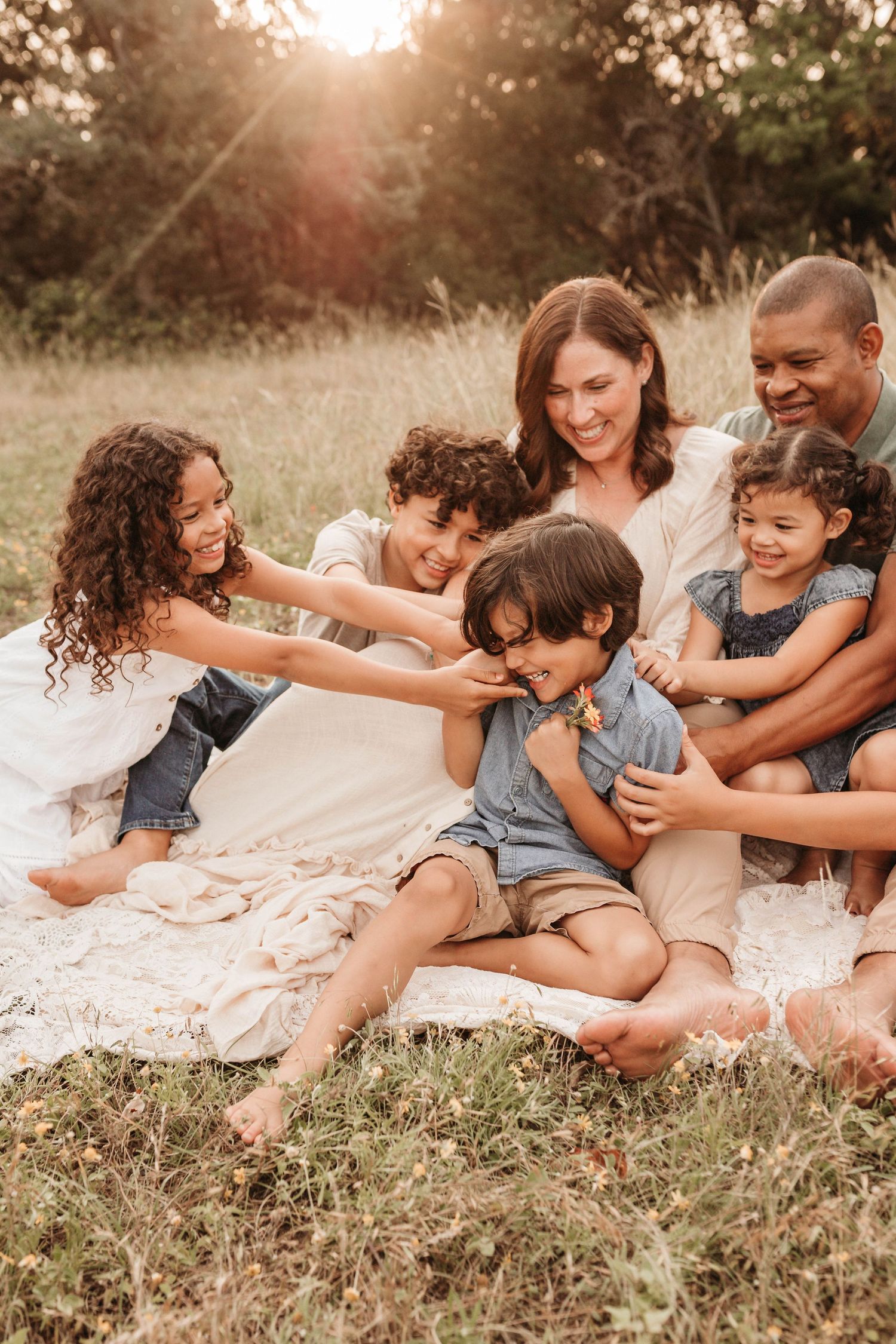 A joyful family lounges together on a grassy hillside during a warm sunset photoshoot.