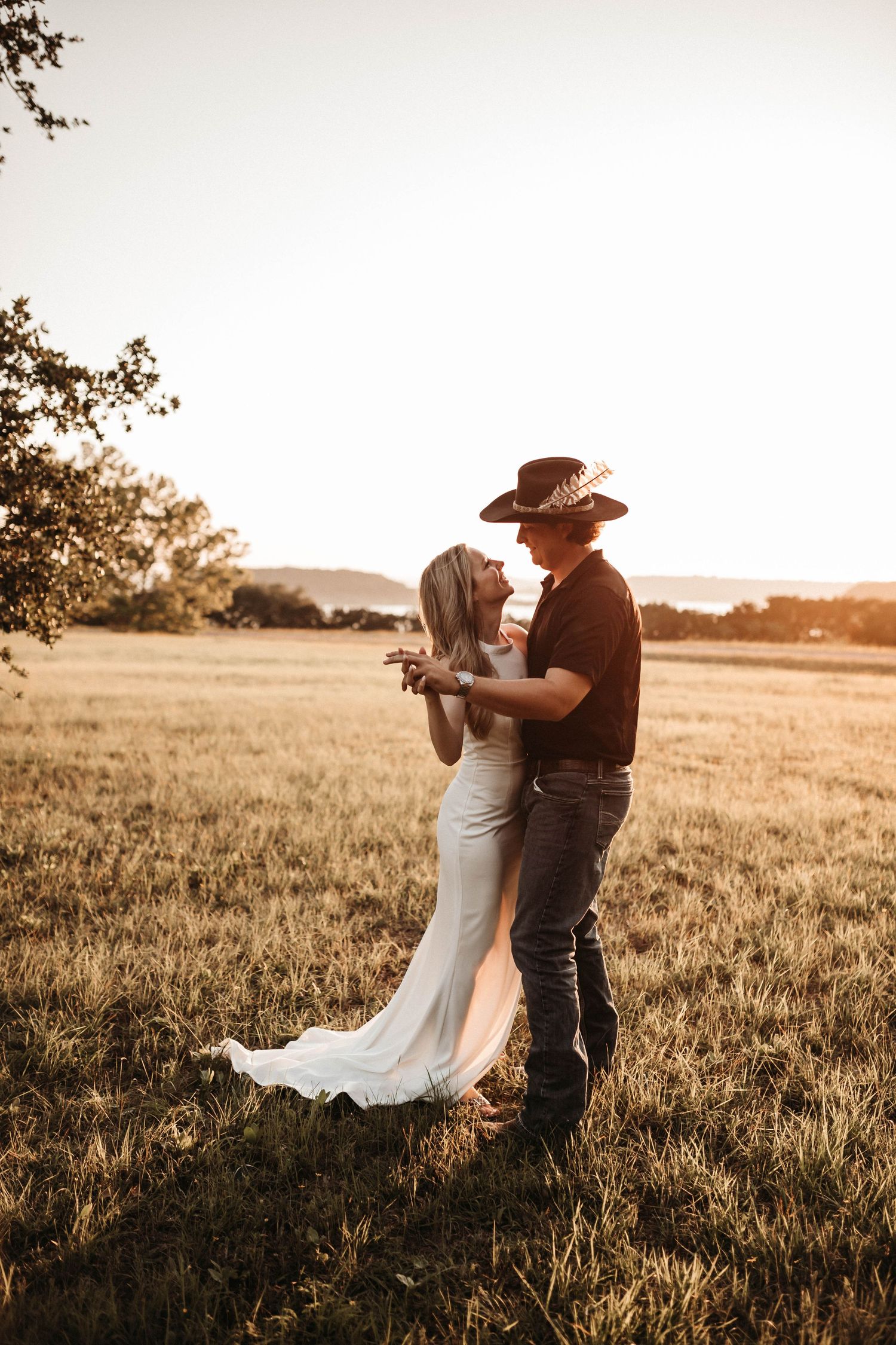 A couple embraces in a golden sunlit field during sunset, creating a romantic silhouette against the rural landscape.