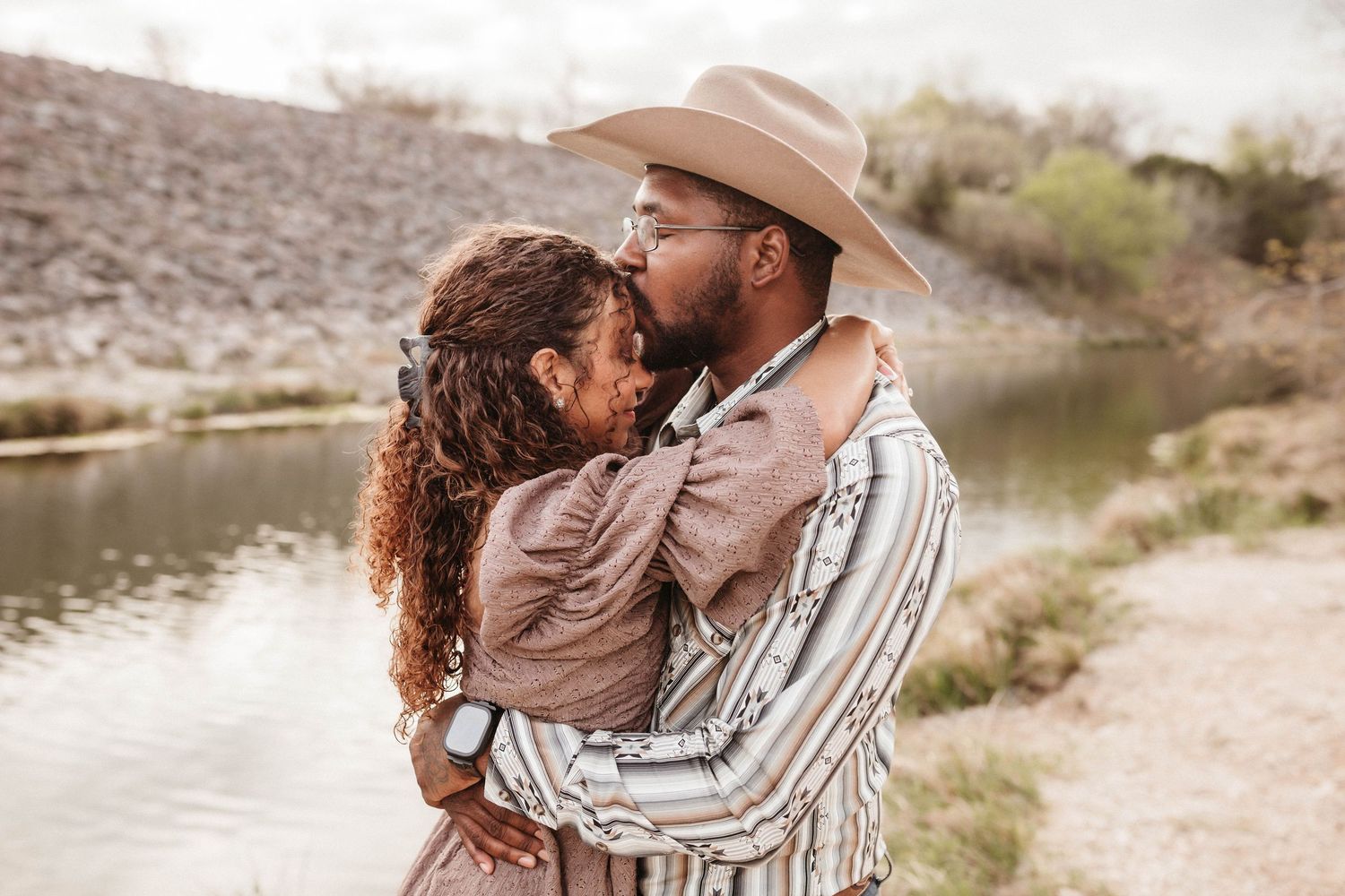 A couple shares a tender moment on a beach during golden hour.