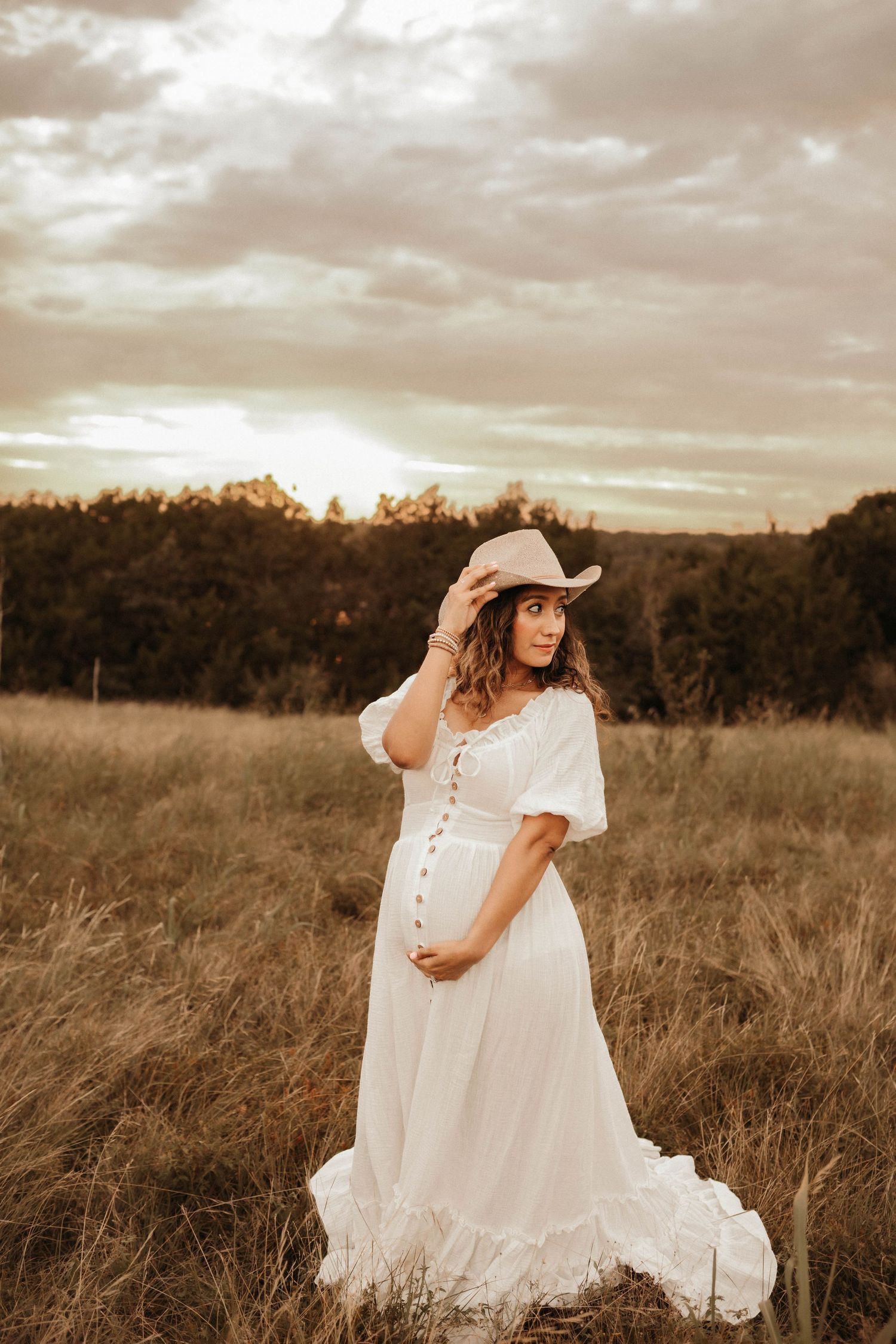 A flowing white dress moves gracefully across a golden field at sunset with dramatic clouds overhead.
