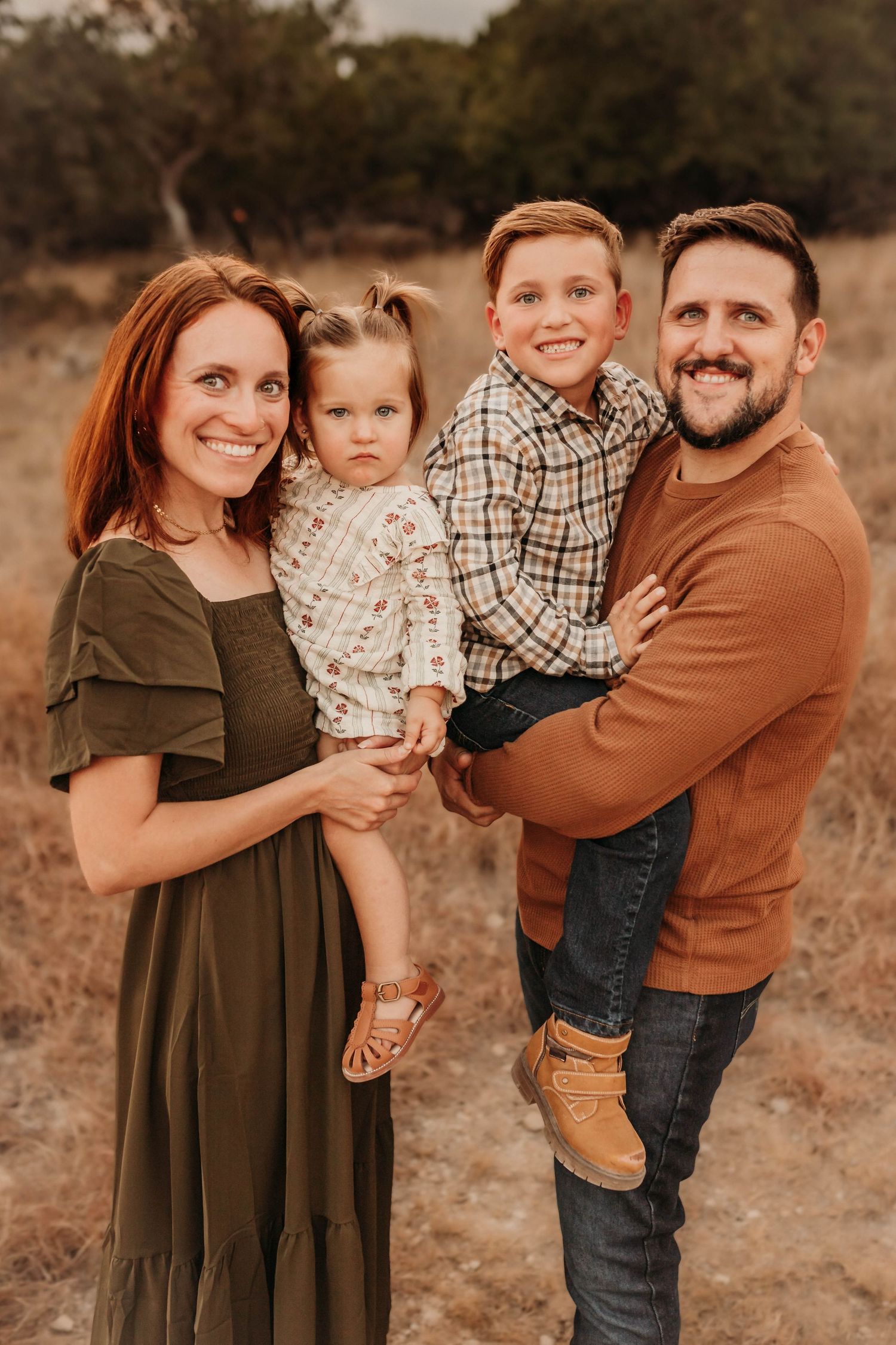 A family in coordinated earth-tone outfits poses together outdoors during a fall photo session at sunset.