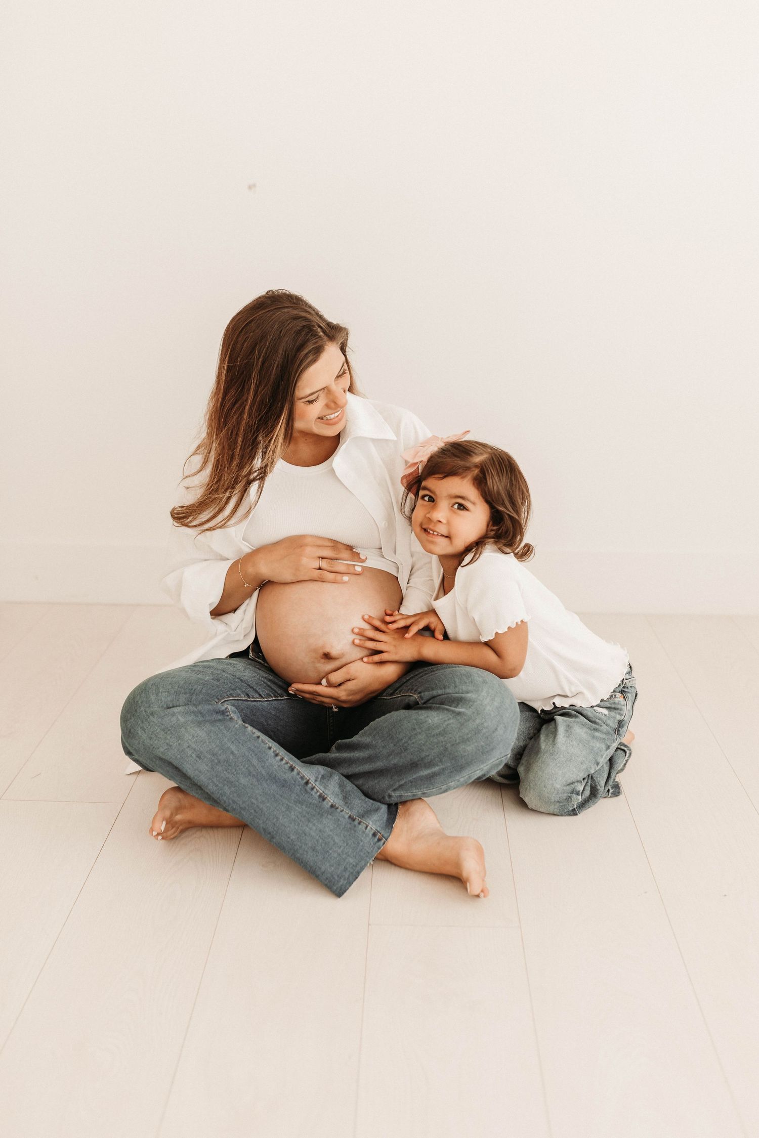 A series of tender maternity photos showing a pregnant woman in white top and jeans embracing with a young child.