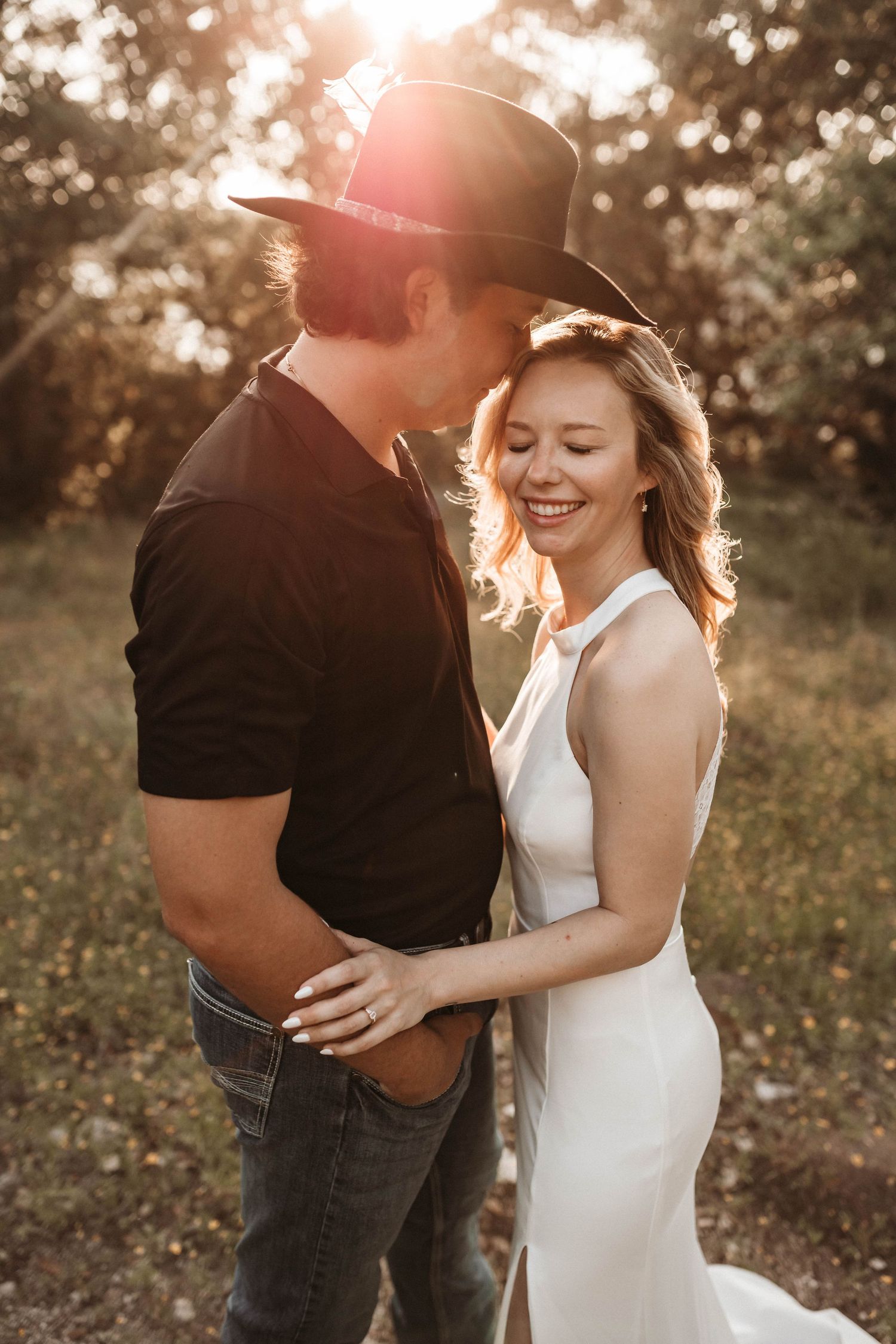 Romantic couple embraces and laughs together during golden hour sunset photoshoot in a natural outdoor setting.