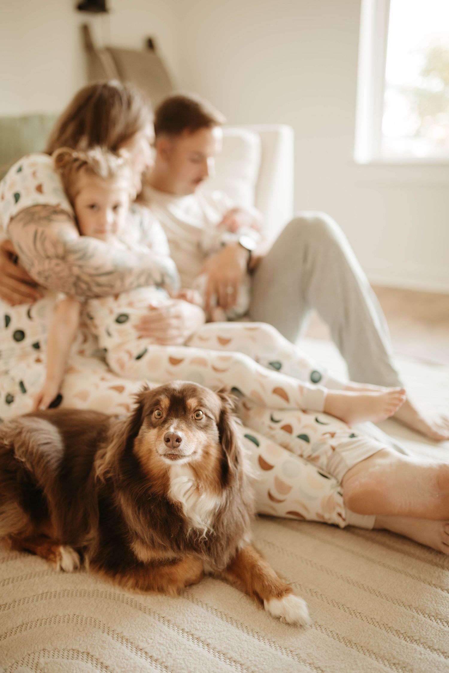 A cozy family scene with a fluffy brown dog relaxing on a bed with people in matching pajamas.