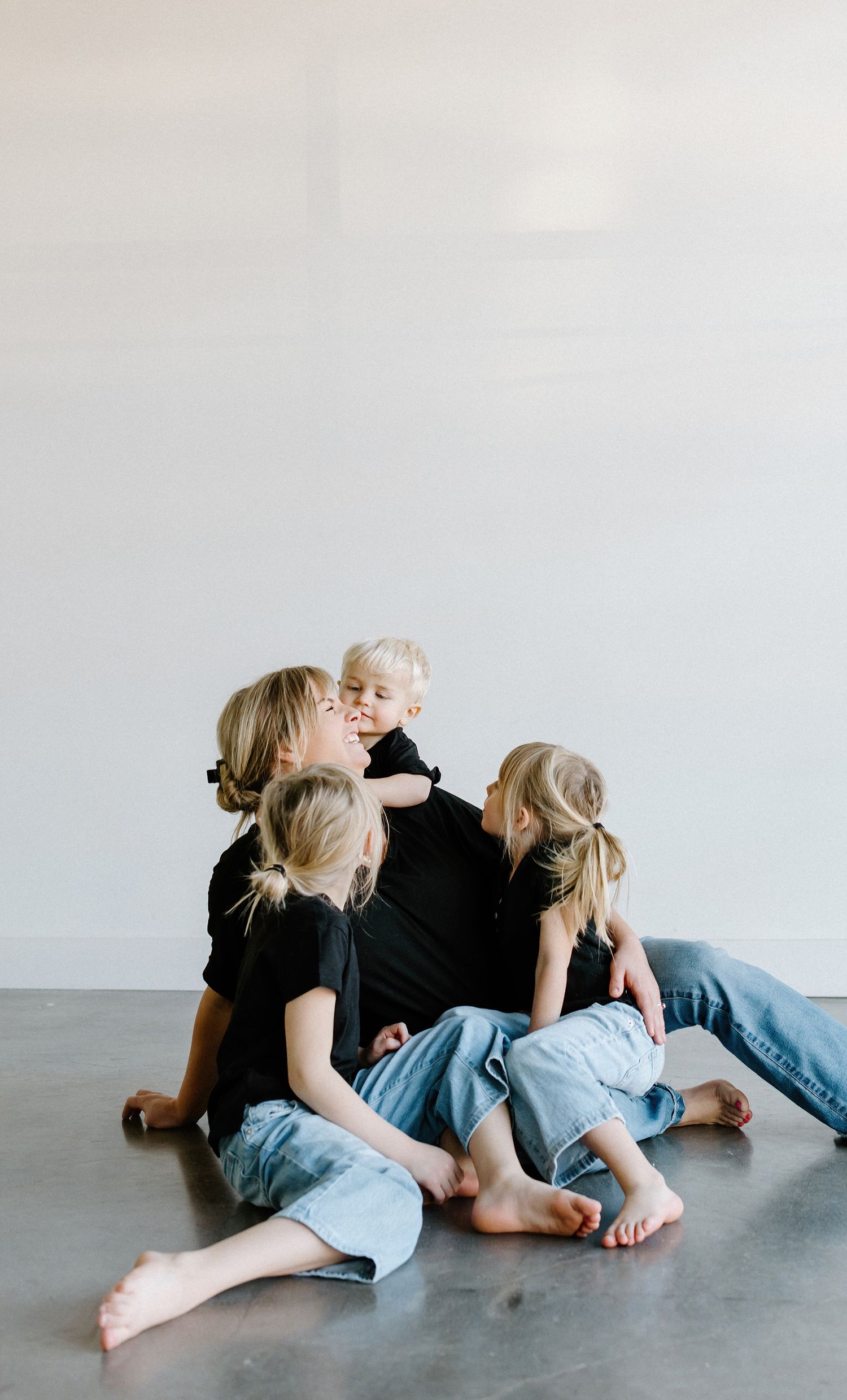 A casual lifestyle portrait of a family sitting together on a grey floor.