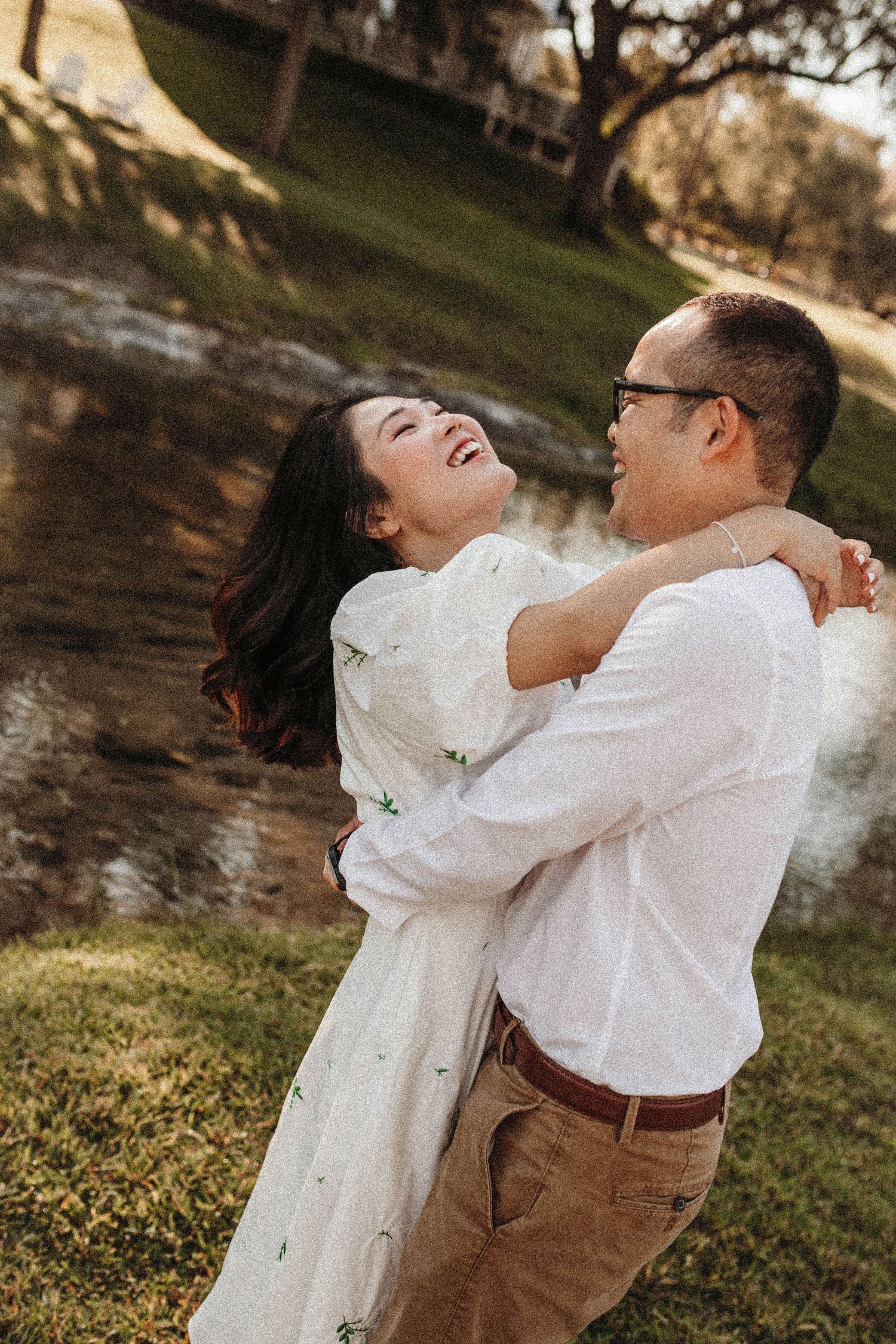 A couple laughs together during a romantic outdoor photoshoot against a natural backdrop.