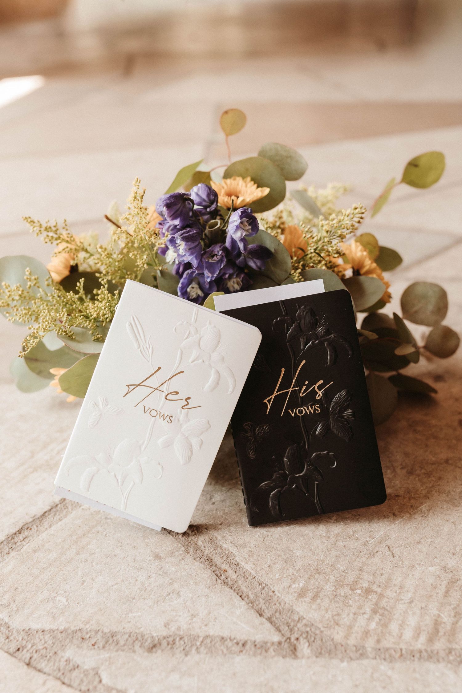 Elegant wedding place cards with black velvet pouches and delicate purple flowers on a textured beige surface.