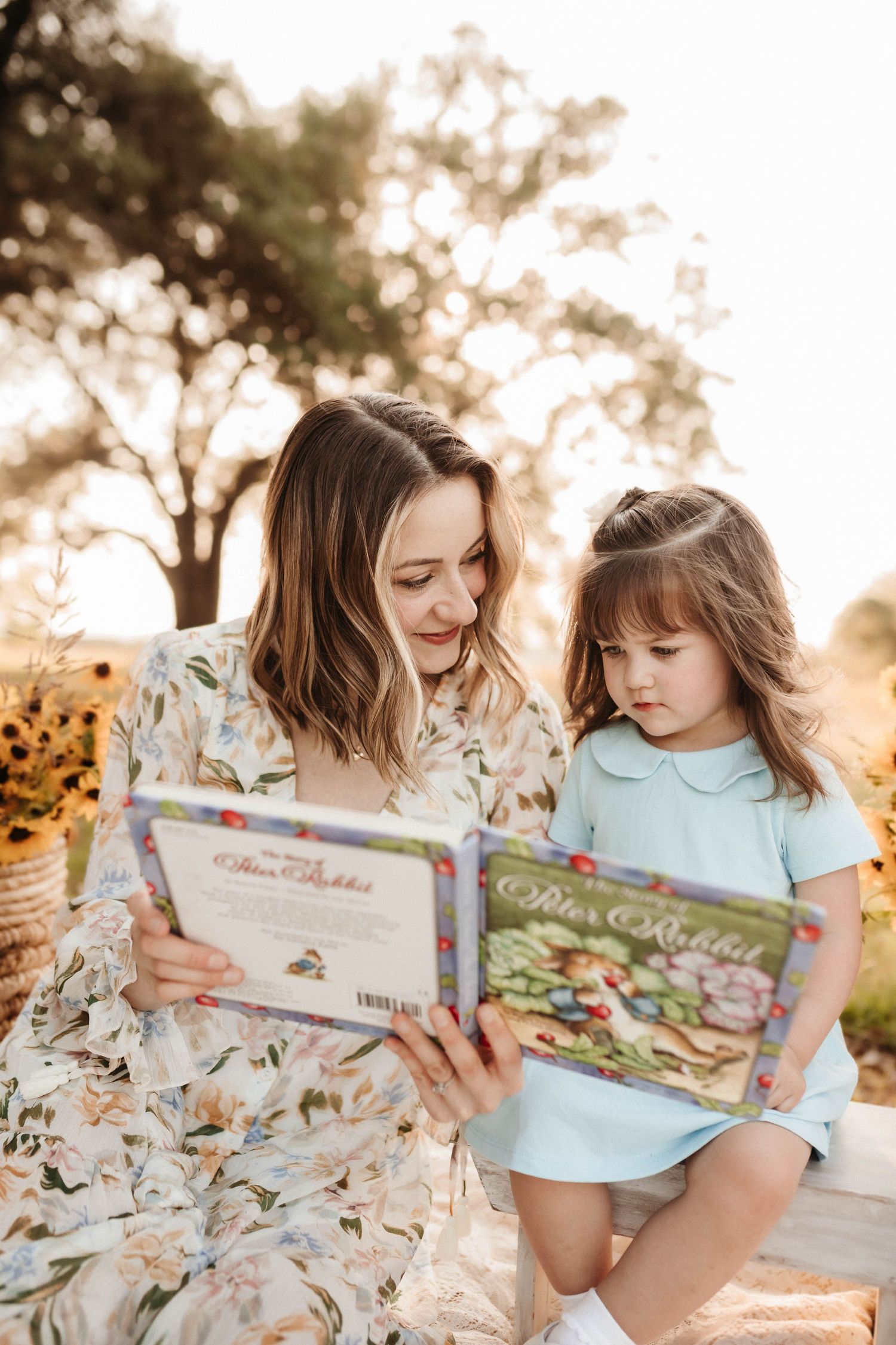 A parent and child share a quiet moment reading a children's book together outdoors during golden hour.