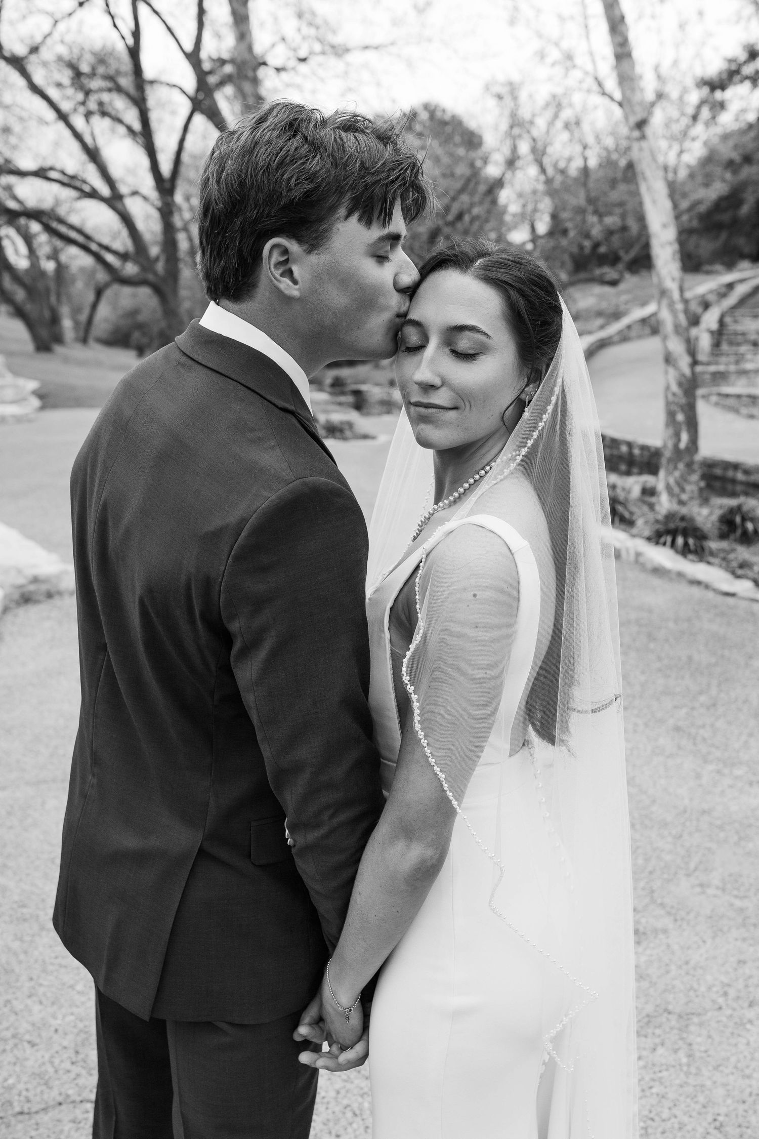 A tender black and white wedding portrait captures an intimate moment between newlyweds in an outdoor setting.