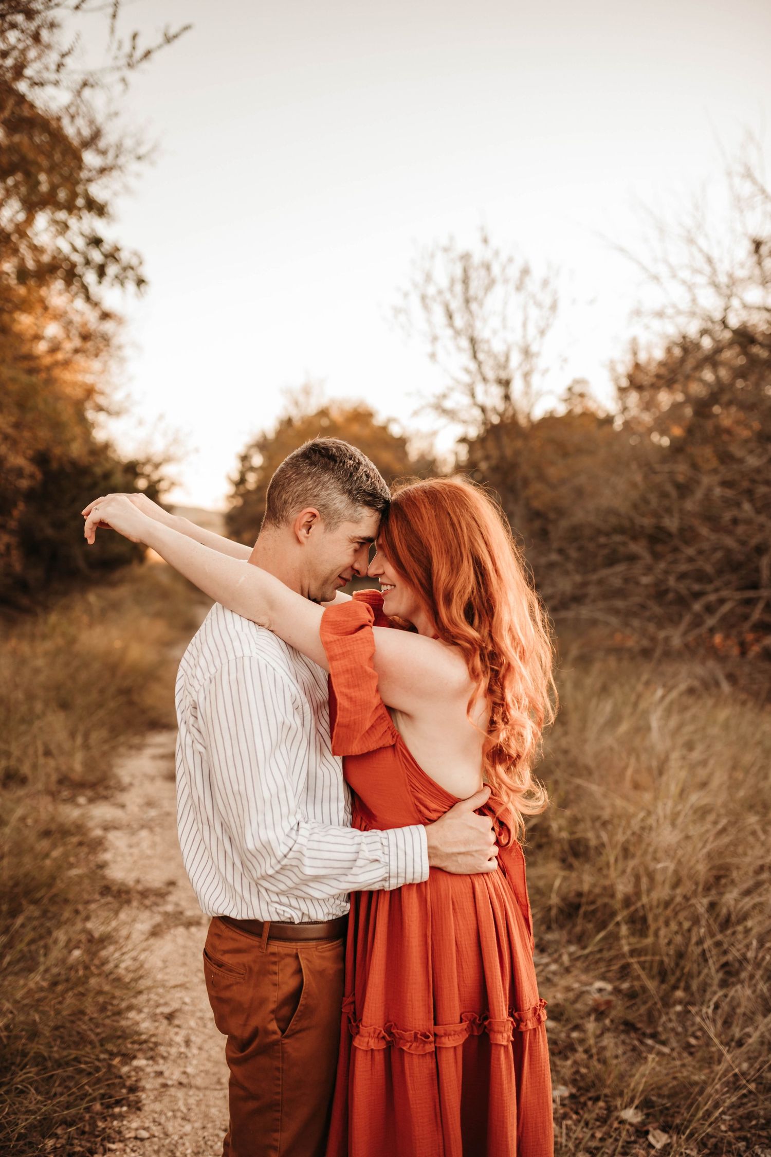 A romantic couple dances together in a rustic outdoor setting during golden hour.