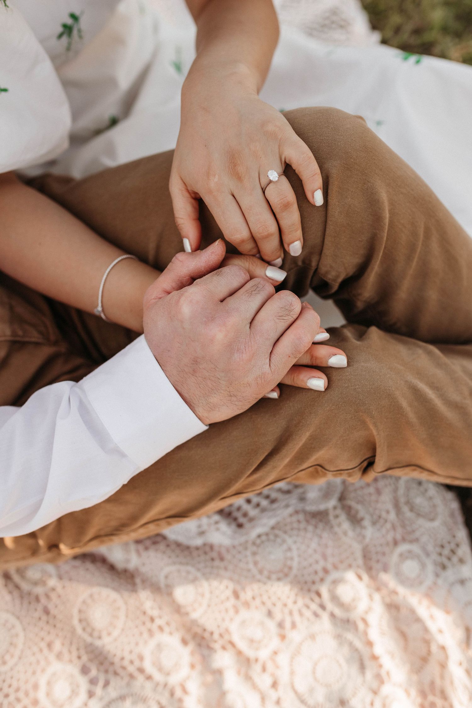 Close-up of intertwined hands resting on lace fabric showing wedding rings.