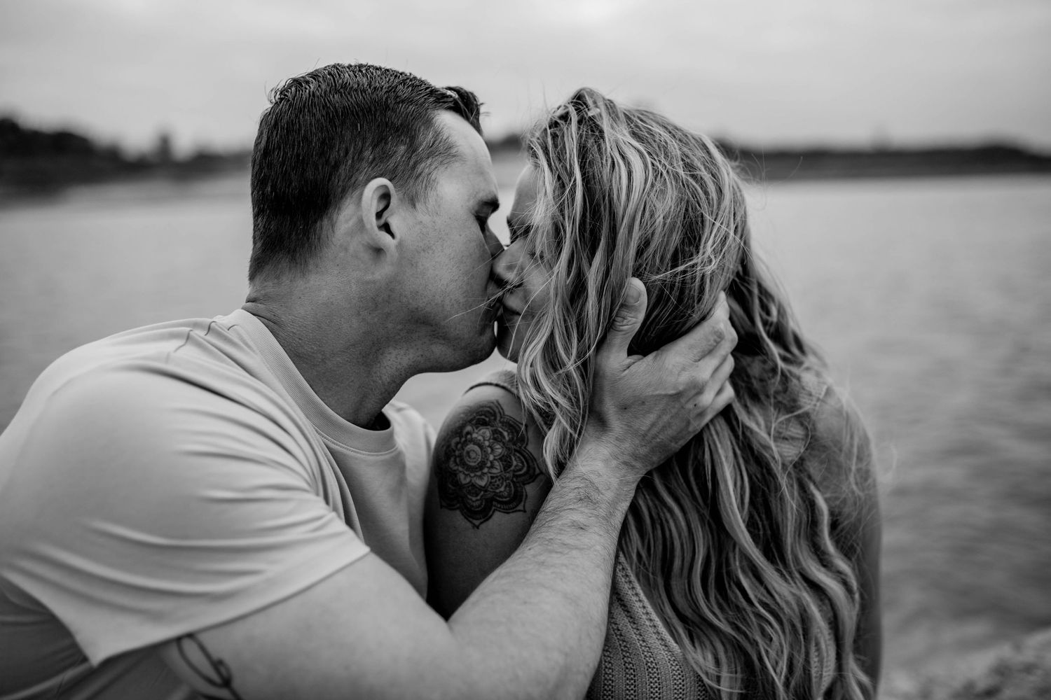 An intimate black and white portrait of a couple by a lake sharing a tender moment.
