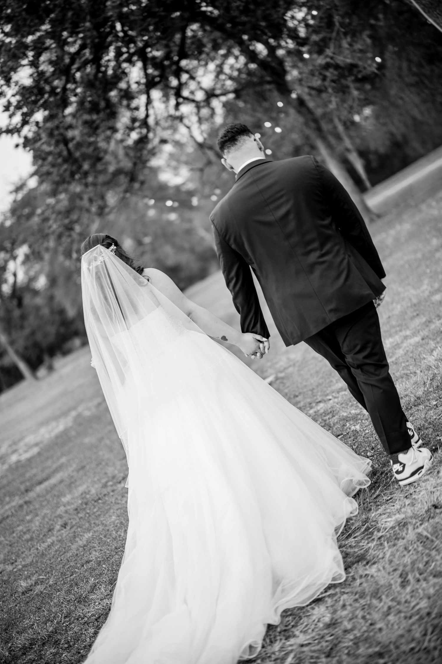 A bride and groom walk hand in hand up a grassy hill in black and white wedding photography.