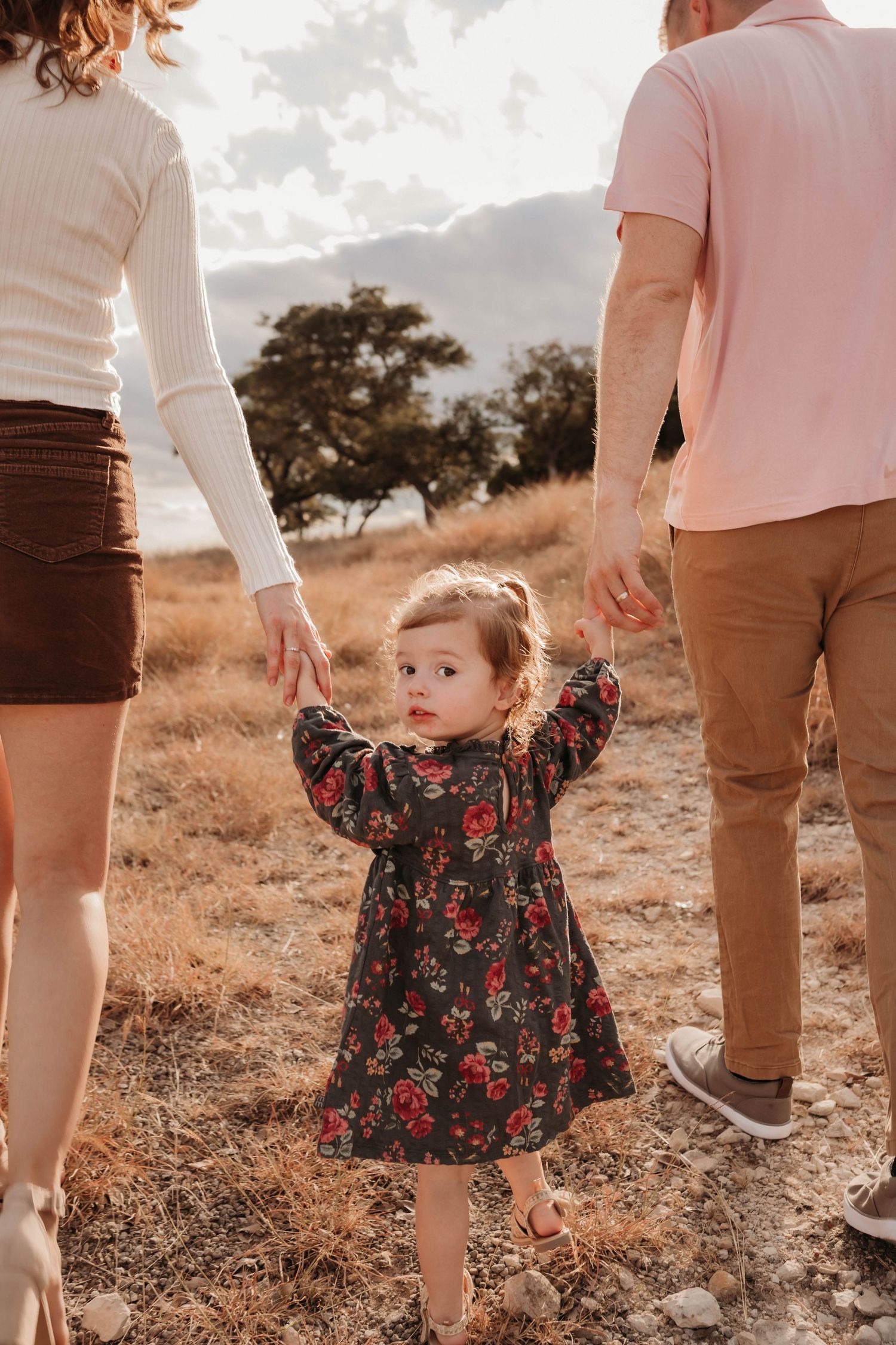 Family walking together on a dusty trail wearing coordinated pink and brown outfits during golden hour.