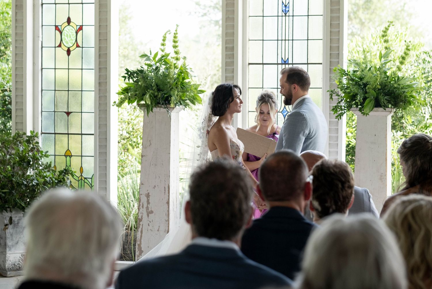 Bride and groom exchange vows at altar in sunlit chapel with stained glass windows.