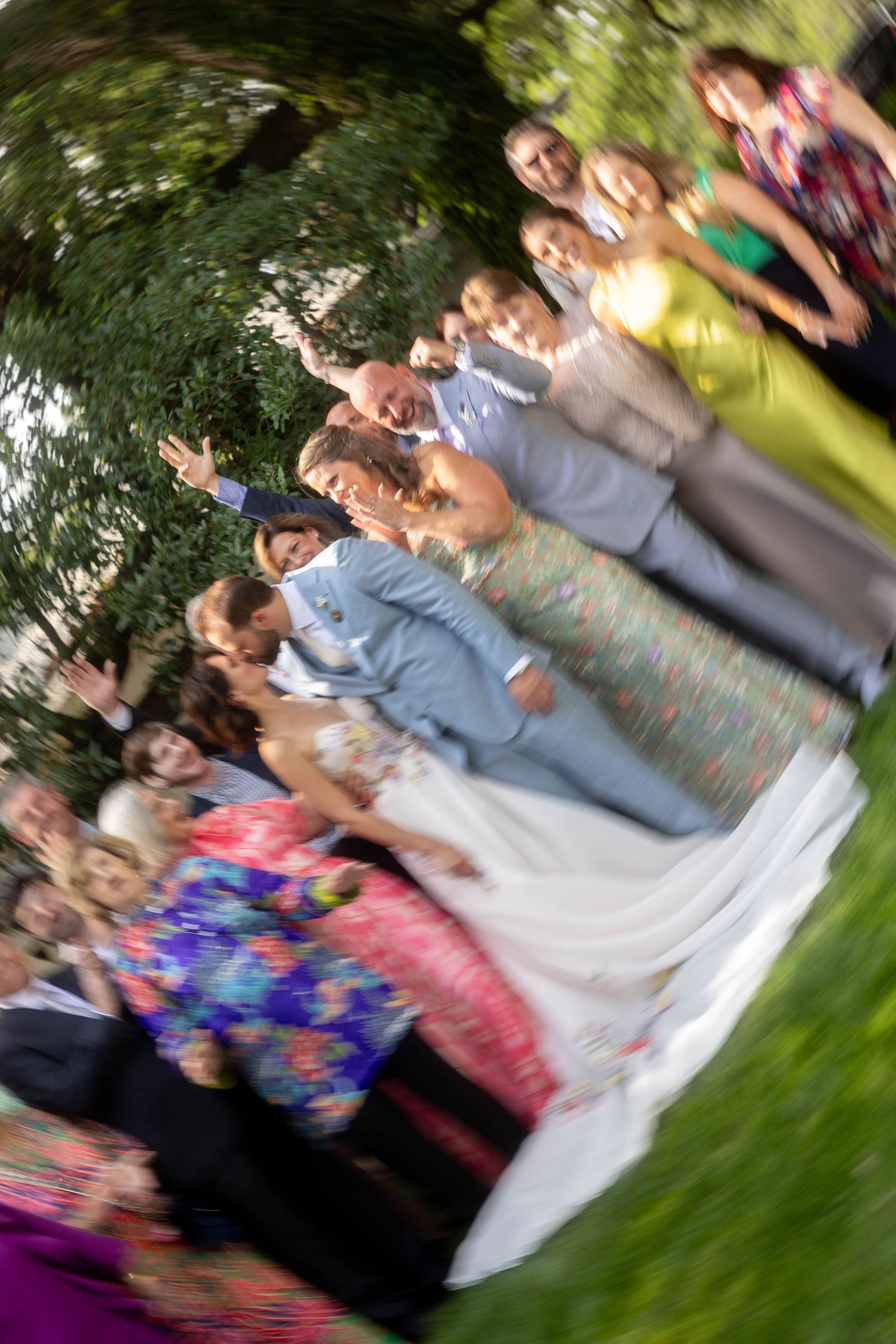 Wedding party and guests celebrate outdoors with a fun spinning photo effect in a garden.
