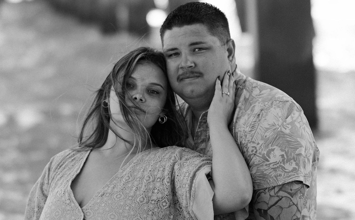 Black and white portrait of young couple embracing tenderly outdoors in soft natural light.