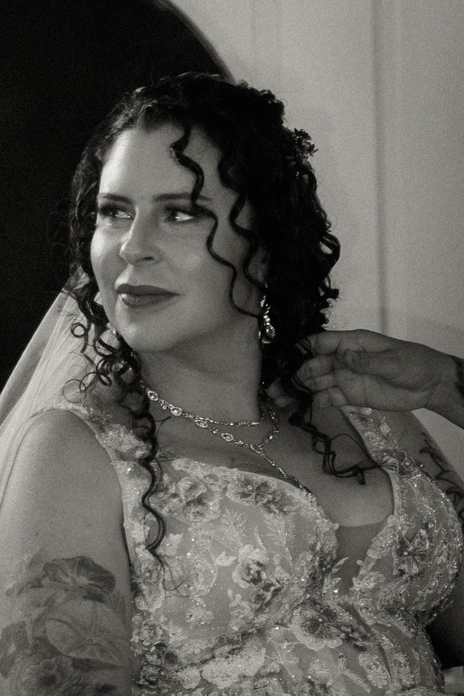 Black and white portrait of curly-haired bride in lace wedding dress with veil and jewelry.