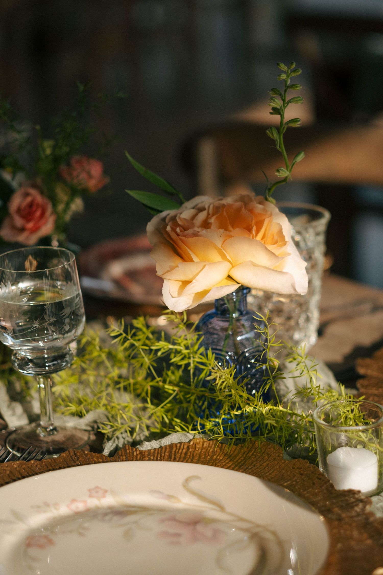 Elegant wedding table setting with a peach rose centerpiece and floral china plate.