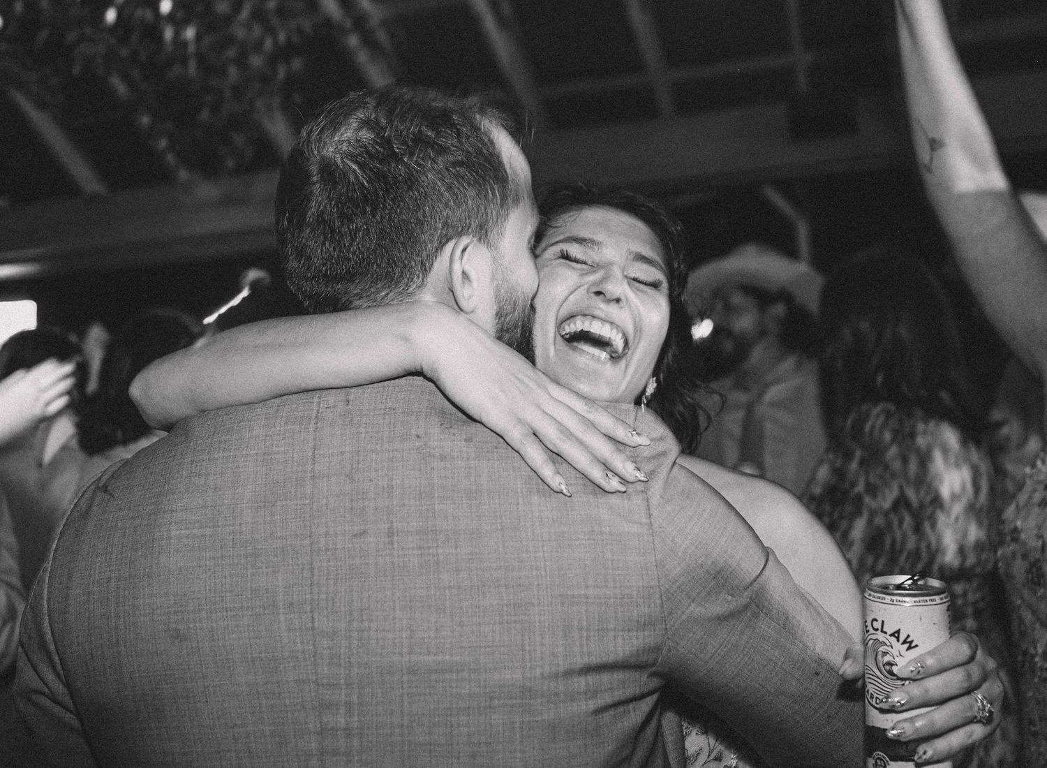 Black and white photo of a joyful woman laughing while embracing a man at a wedding reception.