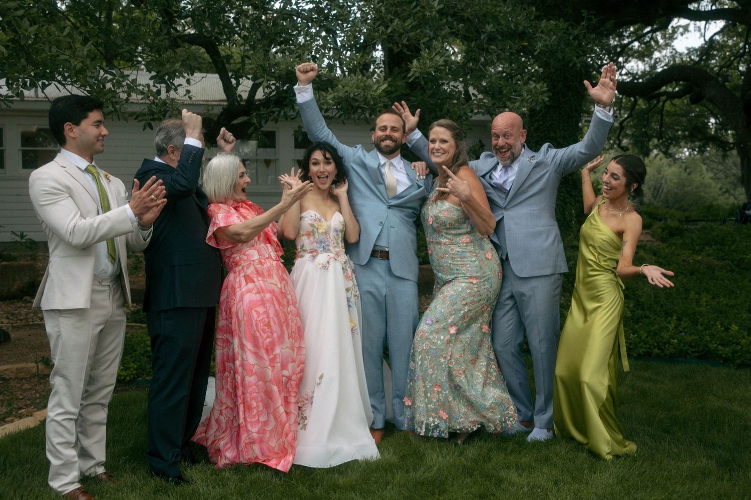 Wedding party celebrating outdoors with bride in floral gown and guests in colorful attire.