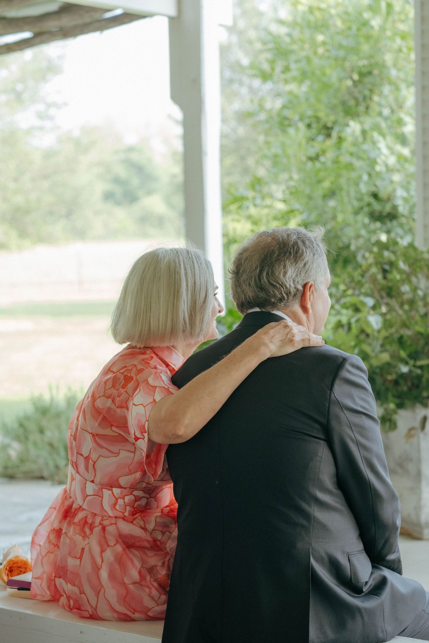 Senior couple in formal attire sitting together gazing out at garden view from porch.