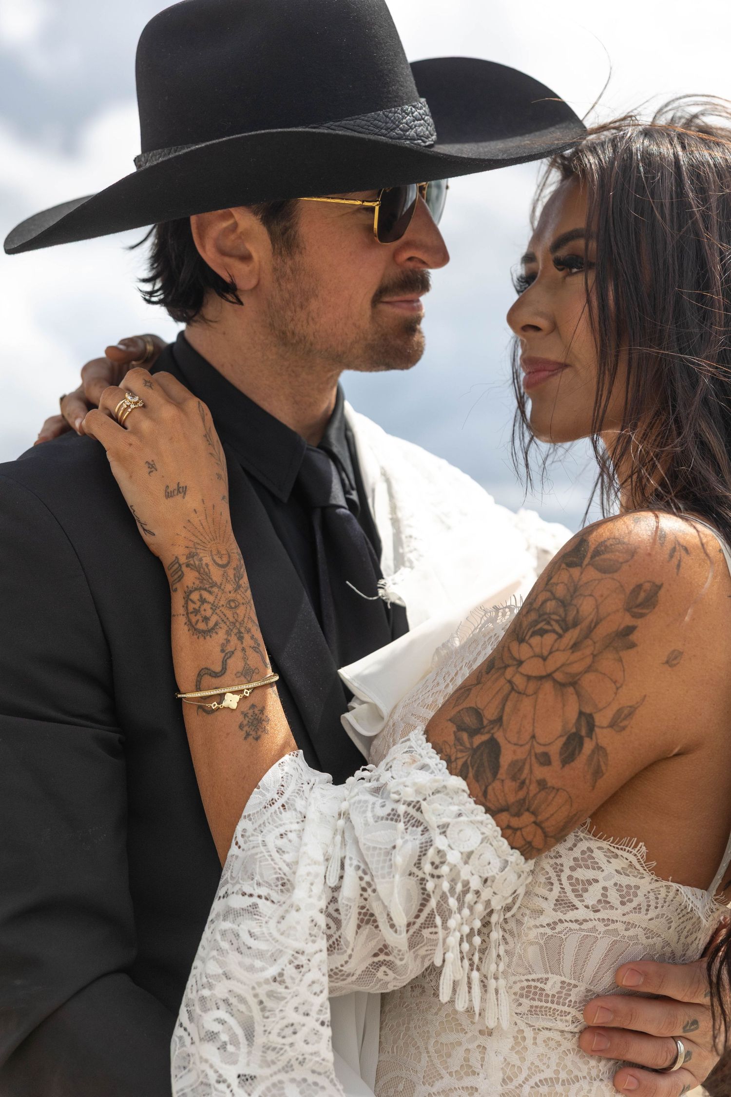 A couple in wedding attire share intimate moments, with the bride wearing a lace dress and showing ornate back tattoos.