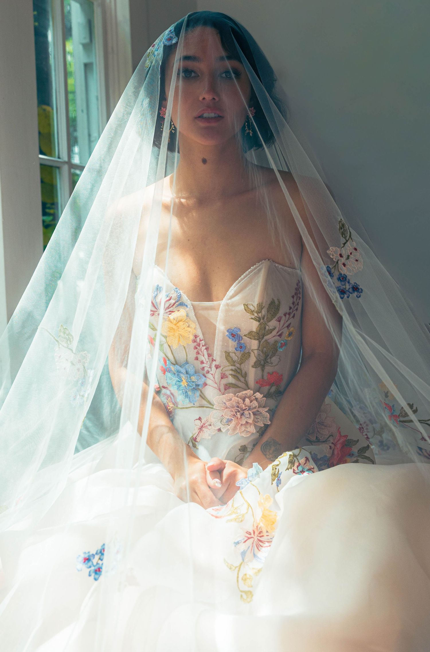 Bride wearing a floral embroidered strapless gown sits draped in a delicate lace veil.