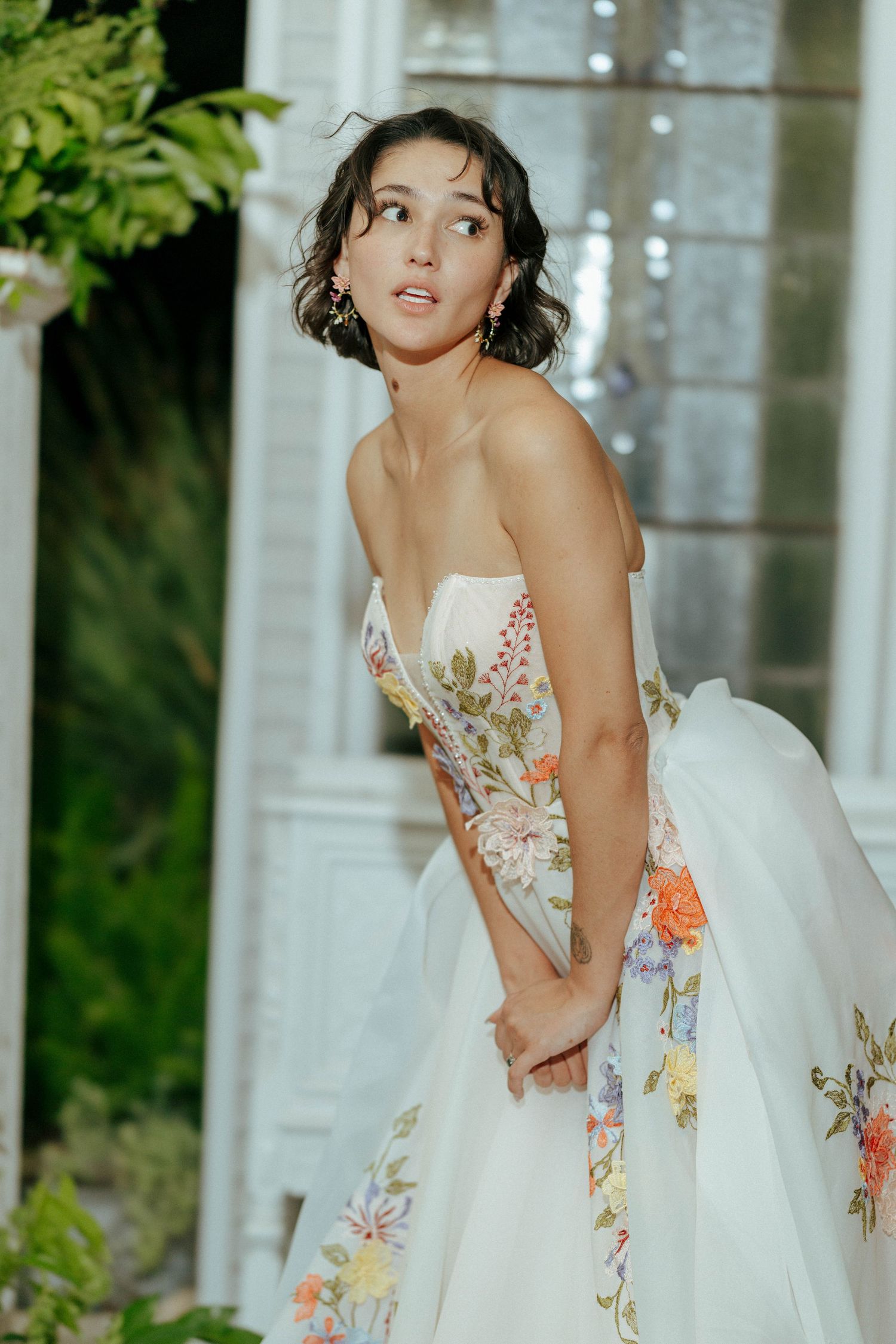 Bride in strapless floral embroidered ball gown posing outdoors near white garden structure.