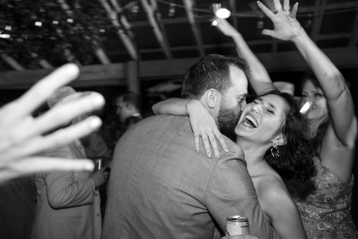 Black and white photo of a joyful couple embracing and dancing at a lively wedding reception on the dance floor.