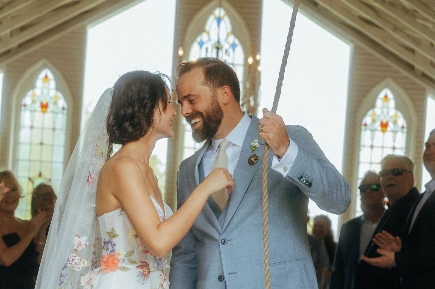 Bride and groom sharing a joyful moment inside a chapel with stained glass windows.