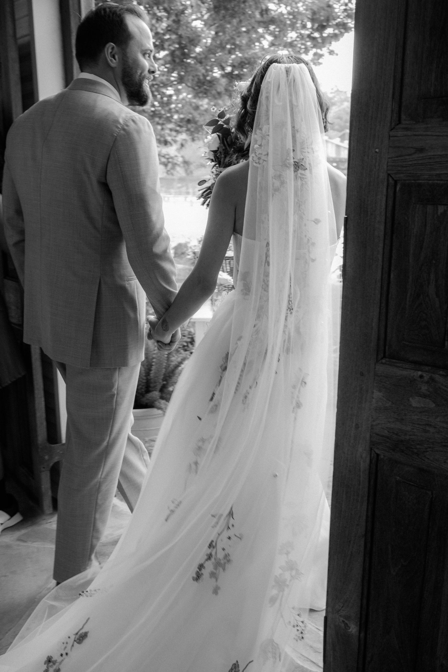 Black and white photo of bride and groom holding hands in a chapel doorway.