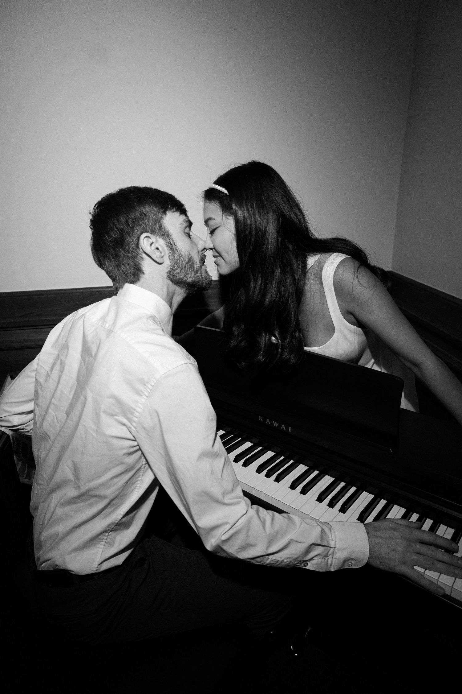 Romantic black and white photo of a couple sharing a kiss at a grand piano.