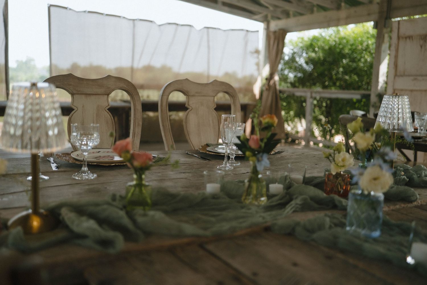 Elegant outdoor wedding table setting with bud vases, candles, and sage green runner.