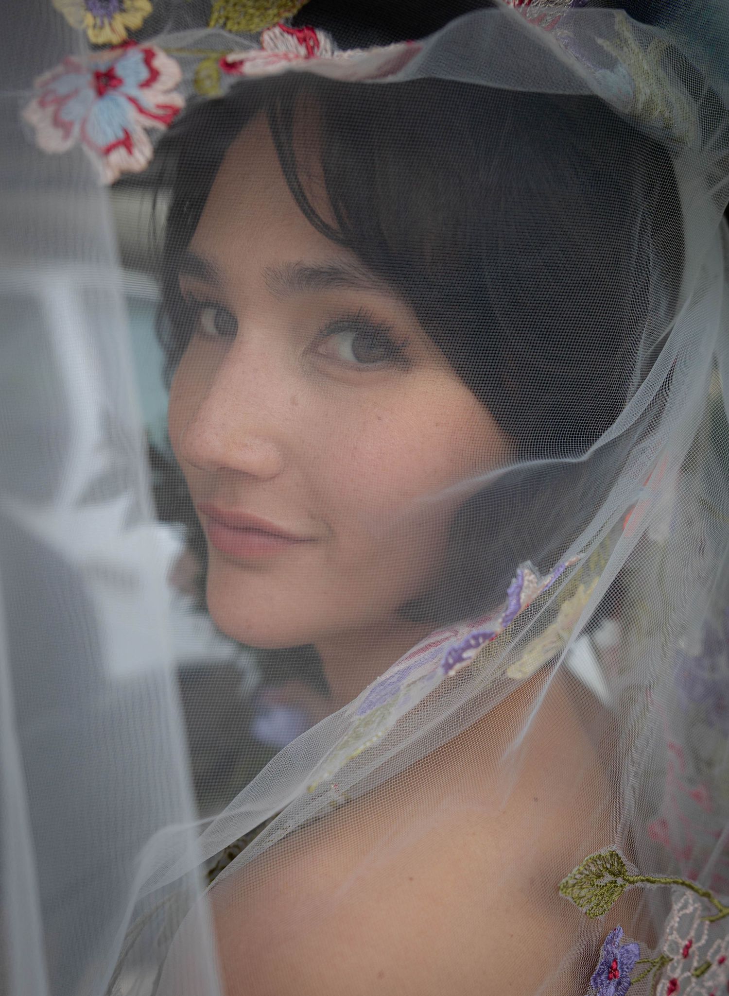 Bride wearing floral veil and embroidered headpiece in soft romantic close-up portrait.