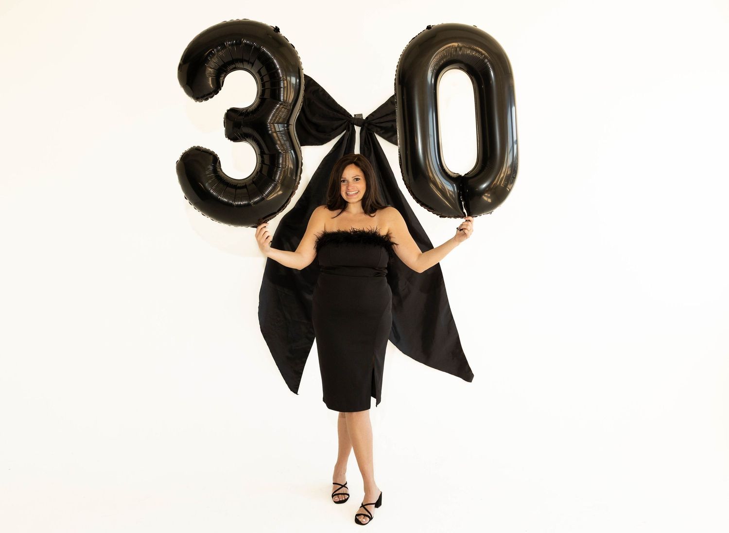 Woman in black dress celebrating her 30th birthday holding large black balloon numbers 3 and 0.