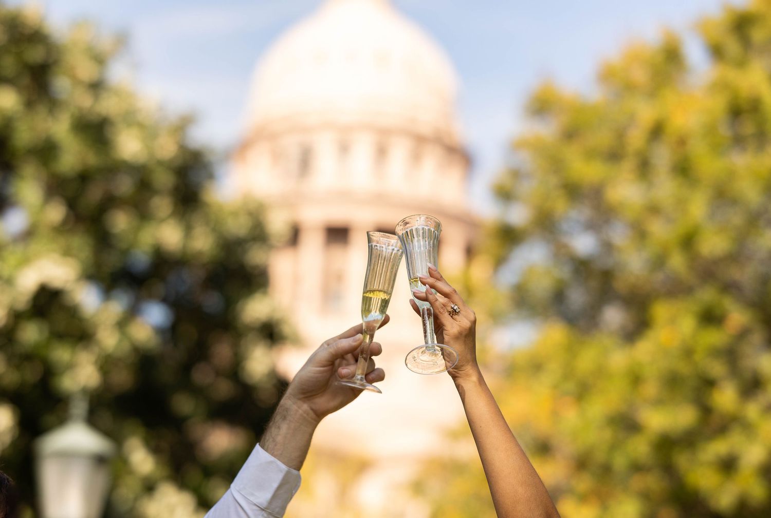 Couple toasting champagne flutes in front of a grand domed capitol building outdoors.