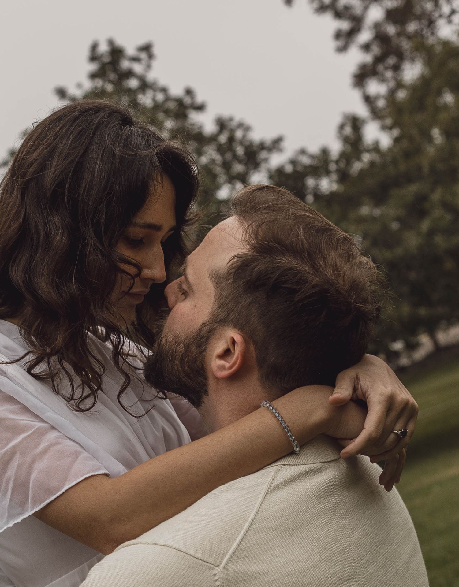 Couple sharing an intimate close moment outdoors, woman smiling while embracing man in a park.