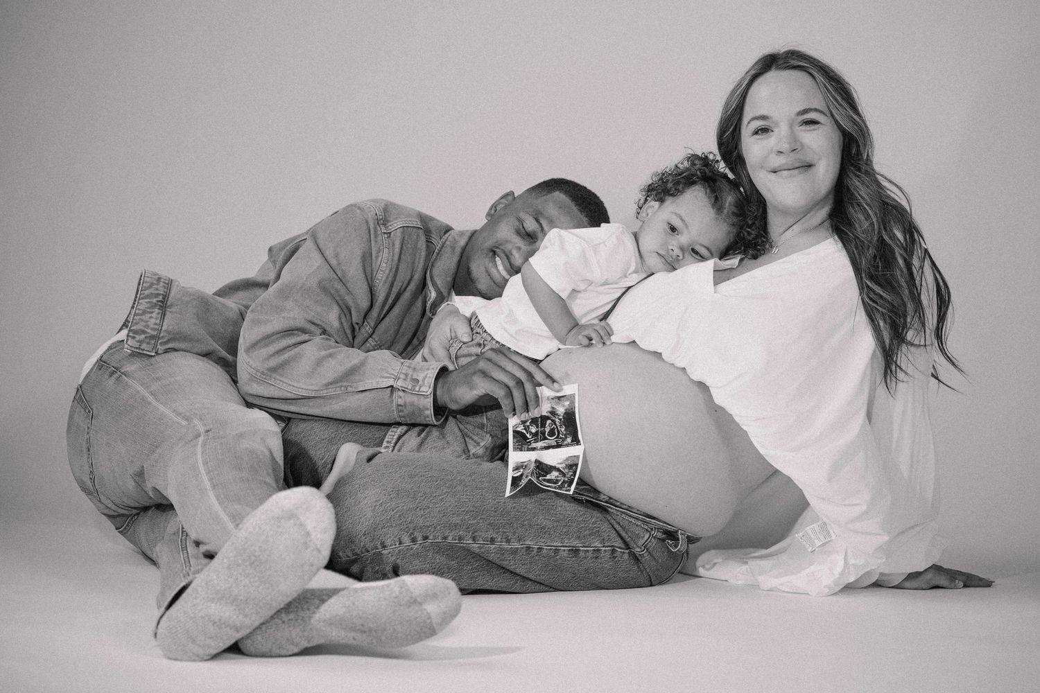 Black and white family maternity photo with couple and toddler holding ultrasound photos on baby bump.