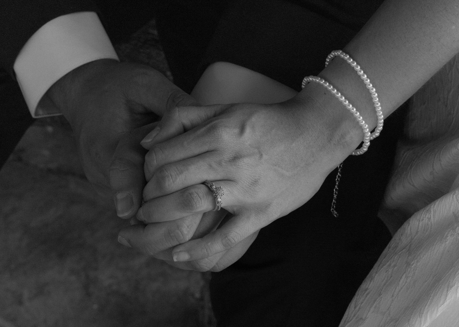 Black and white close-up of hands holding each other in a tender embrace during a wedding ceremony.