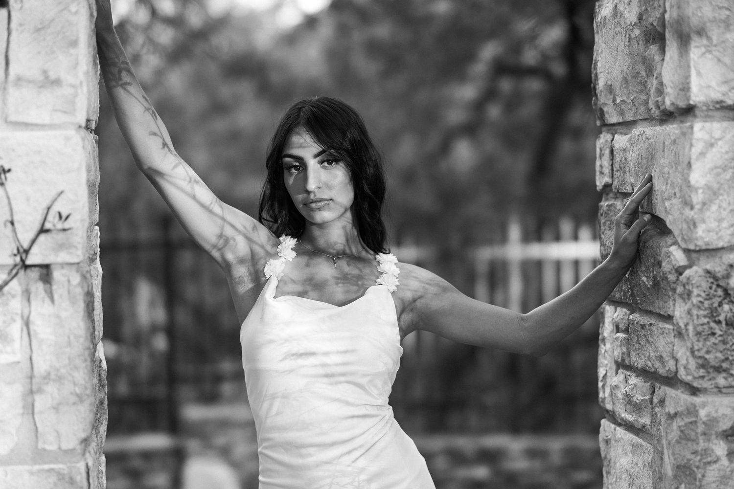Black and white portrait of woman in white dress posing between stone pillars outdoors.