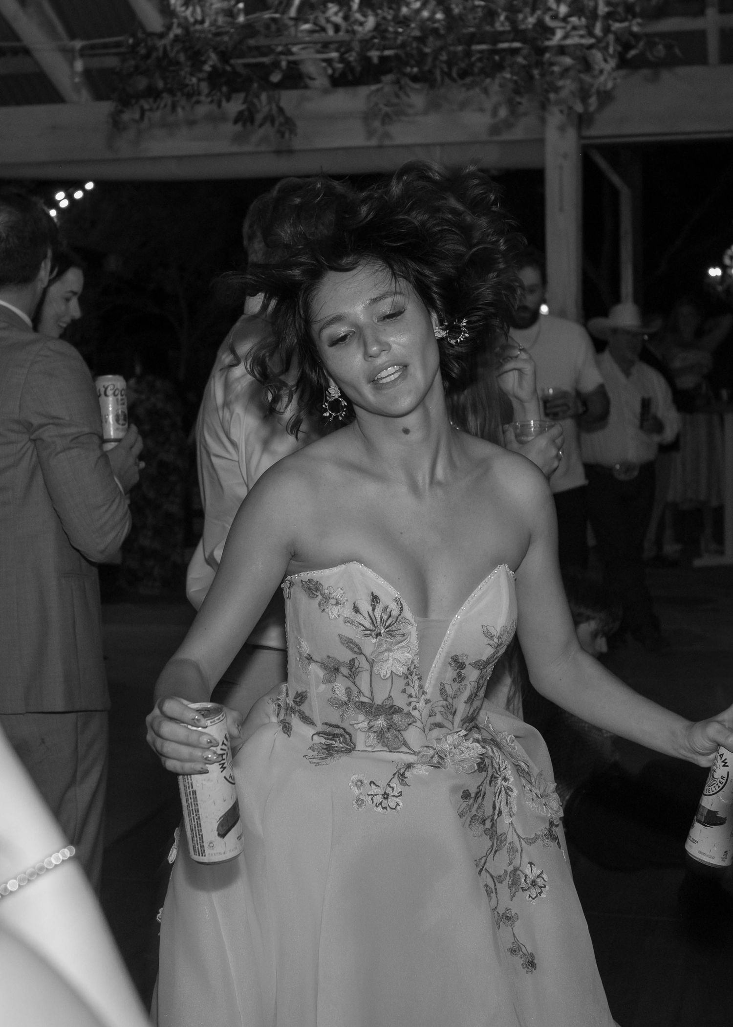 Bride in floral strapless gown dances freely with flowing hair in black and white wedding reception photo.