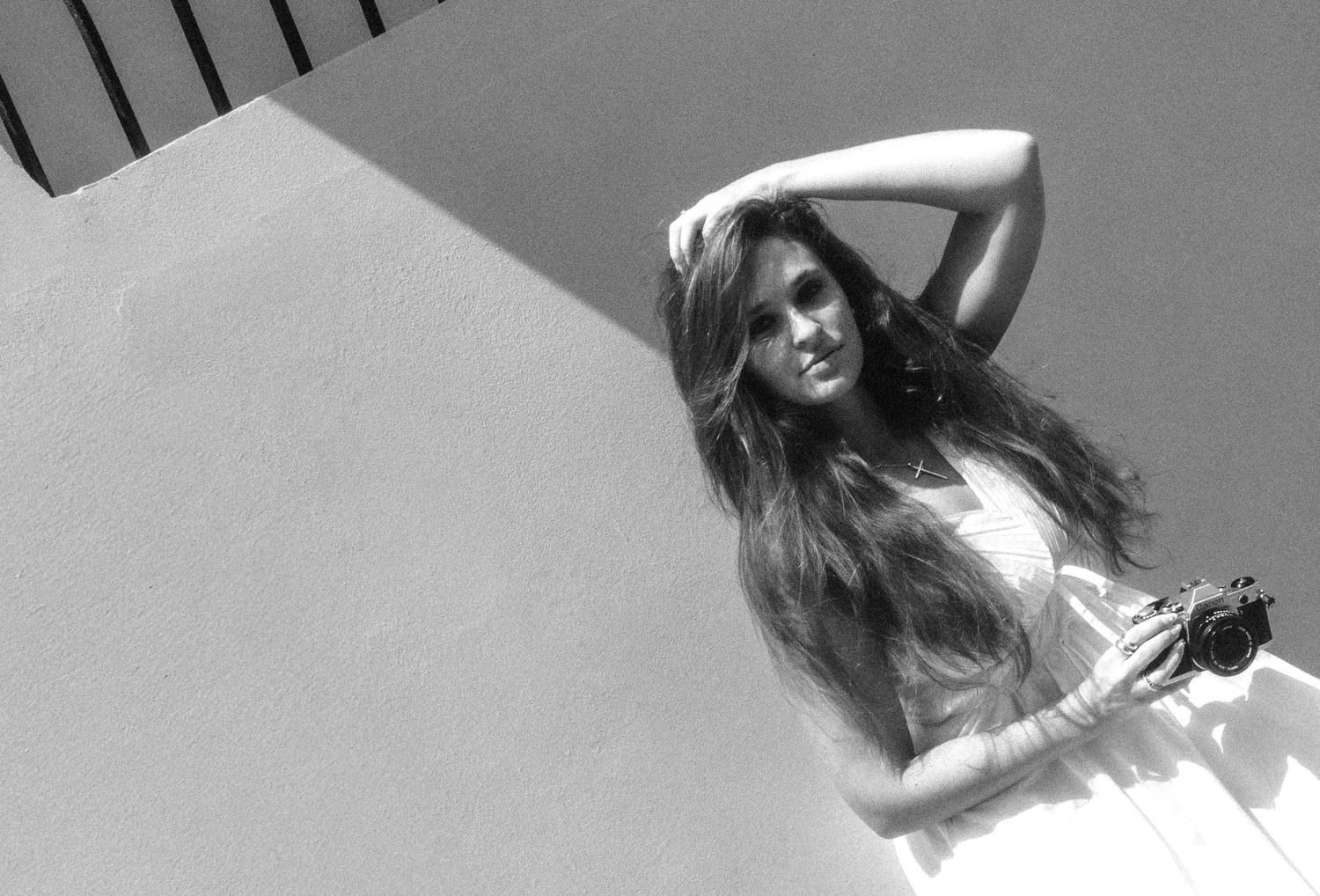 Black and white artistic photo of a woman in a white dress posing against a sunlit wall.