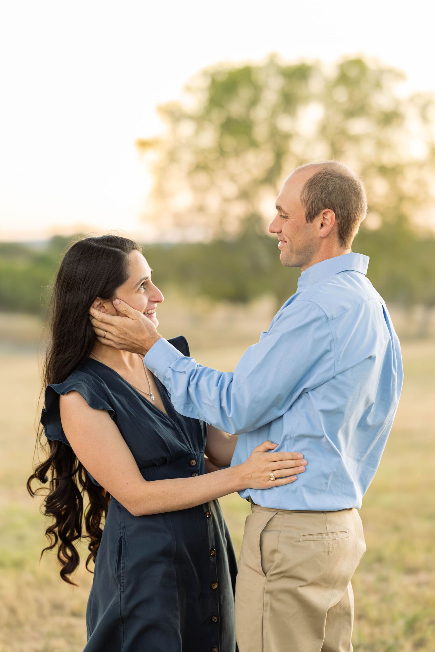 Couple sharing a tender moment in a golden field, man gently cupping woman's face as they gaze into each other's eyes.