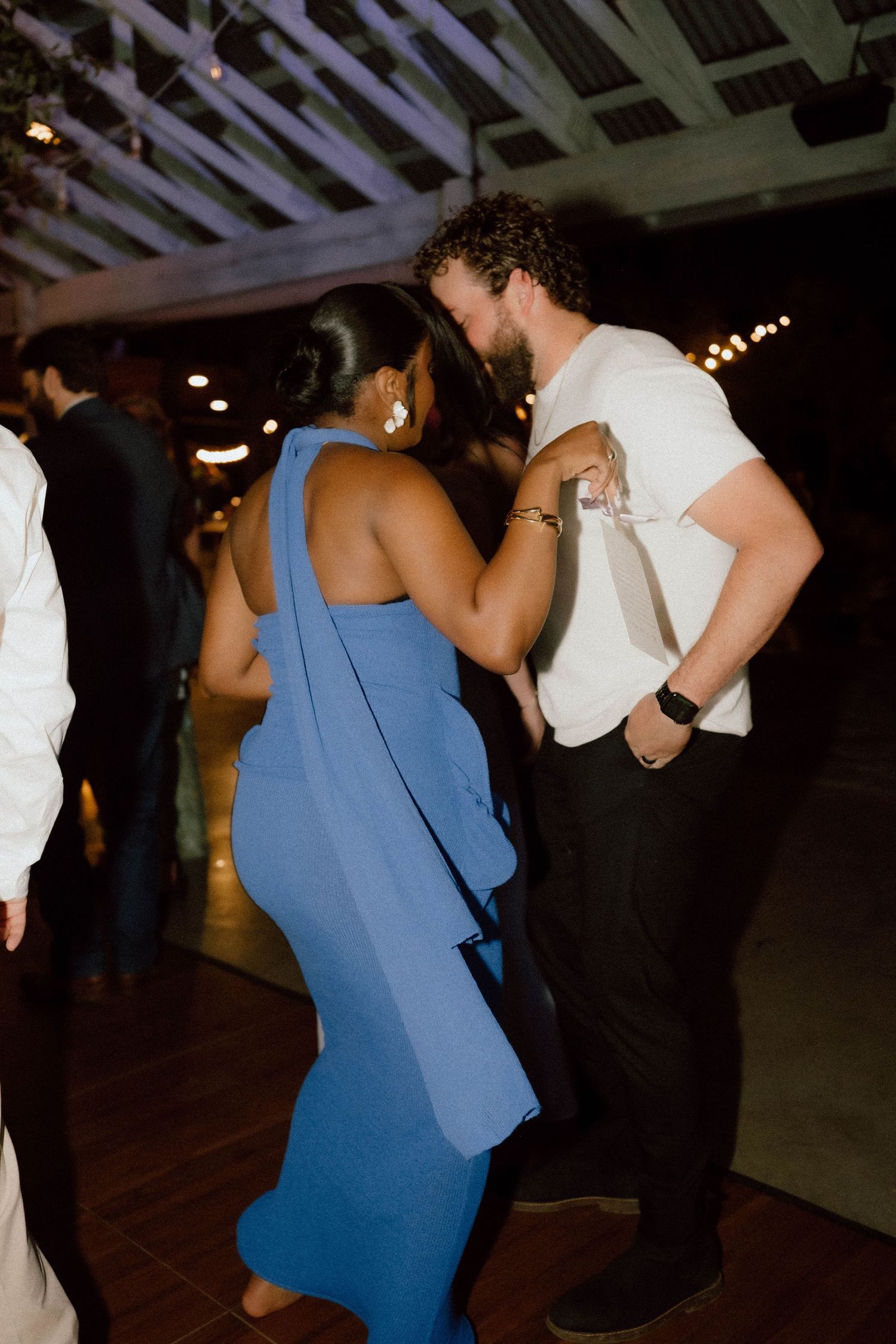 Couple dancing closely together at evening wedding reception under string lights.