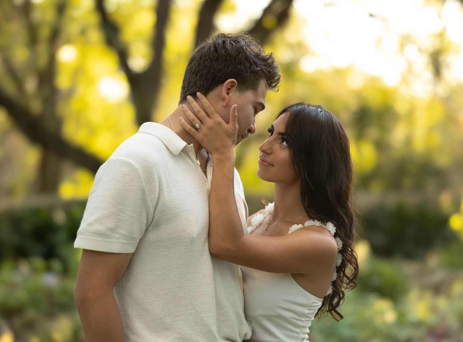 Couple gazing into each other's eyes in a golden sunlit garden.