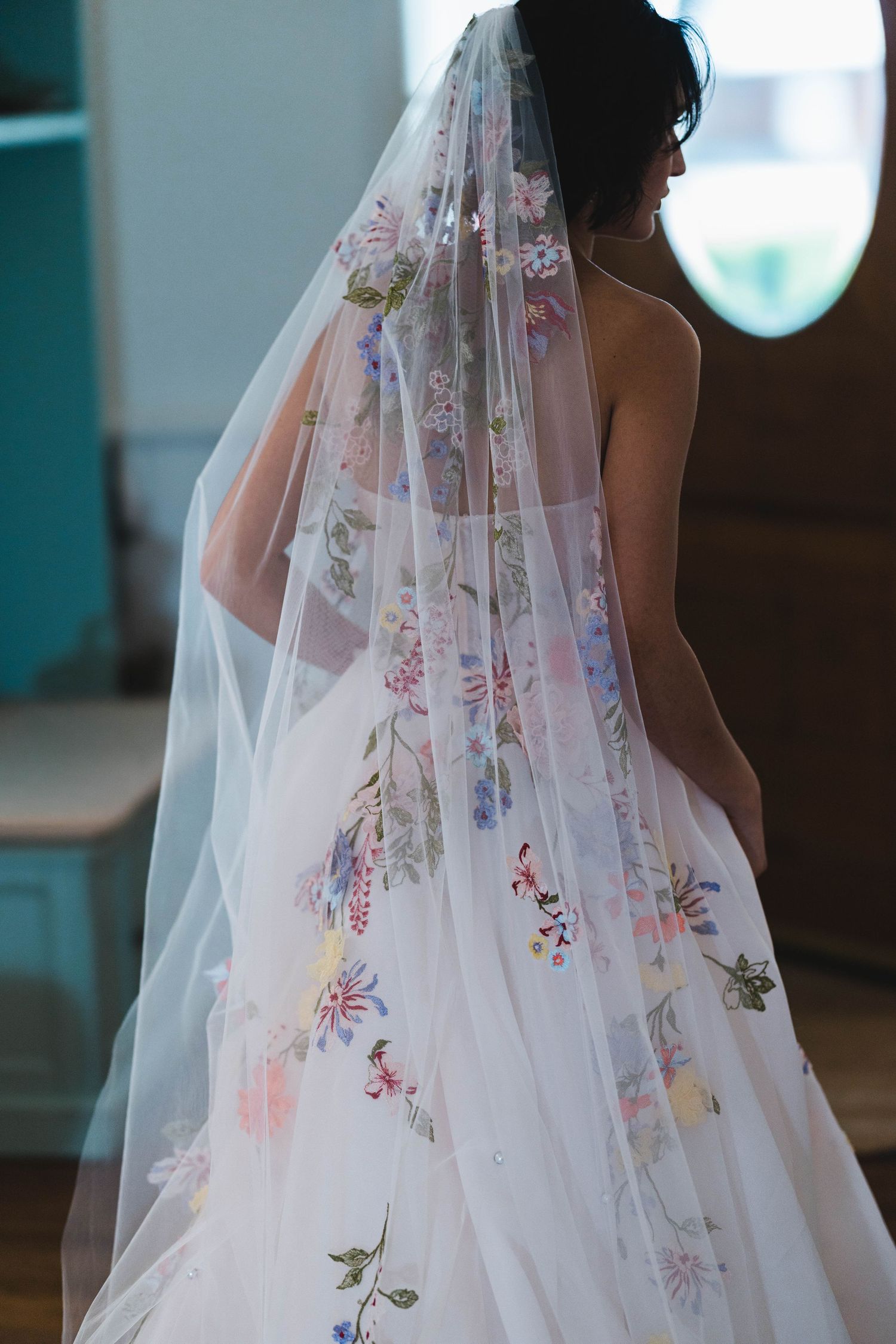 Back view of a bride wearing a stunning floral embroidered wedding veil with colorful botanical details.