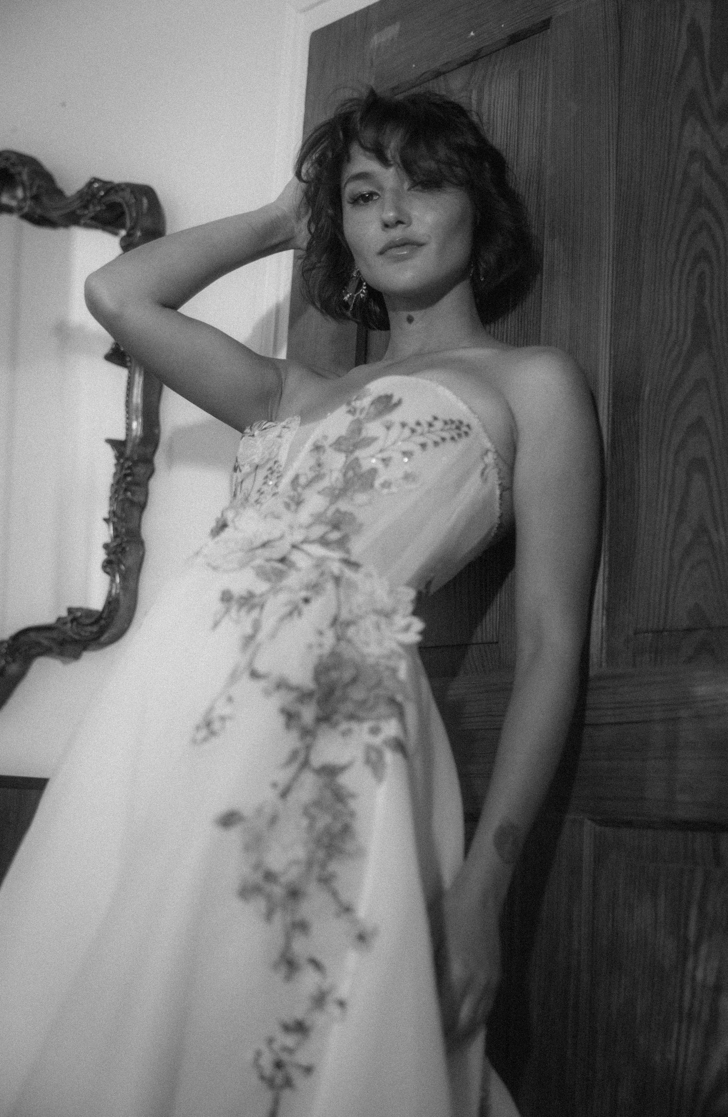 Black and white portrait of a bride in a strapless floral embroidered wedding gown by a wooden door.