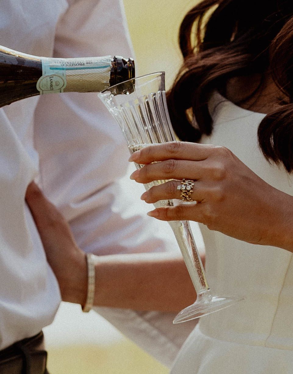 Close-up of bride holding champagne flute with engagement ring while champagne is poured.